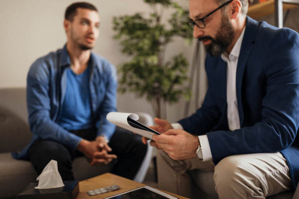 Untitled design - 2024-08-21T144755.058 a man discussing ptsd treatment with his therapist doesn't have to suffer in silence and shares feelings while they are seated.